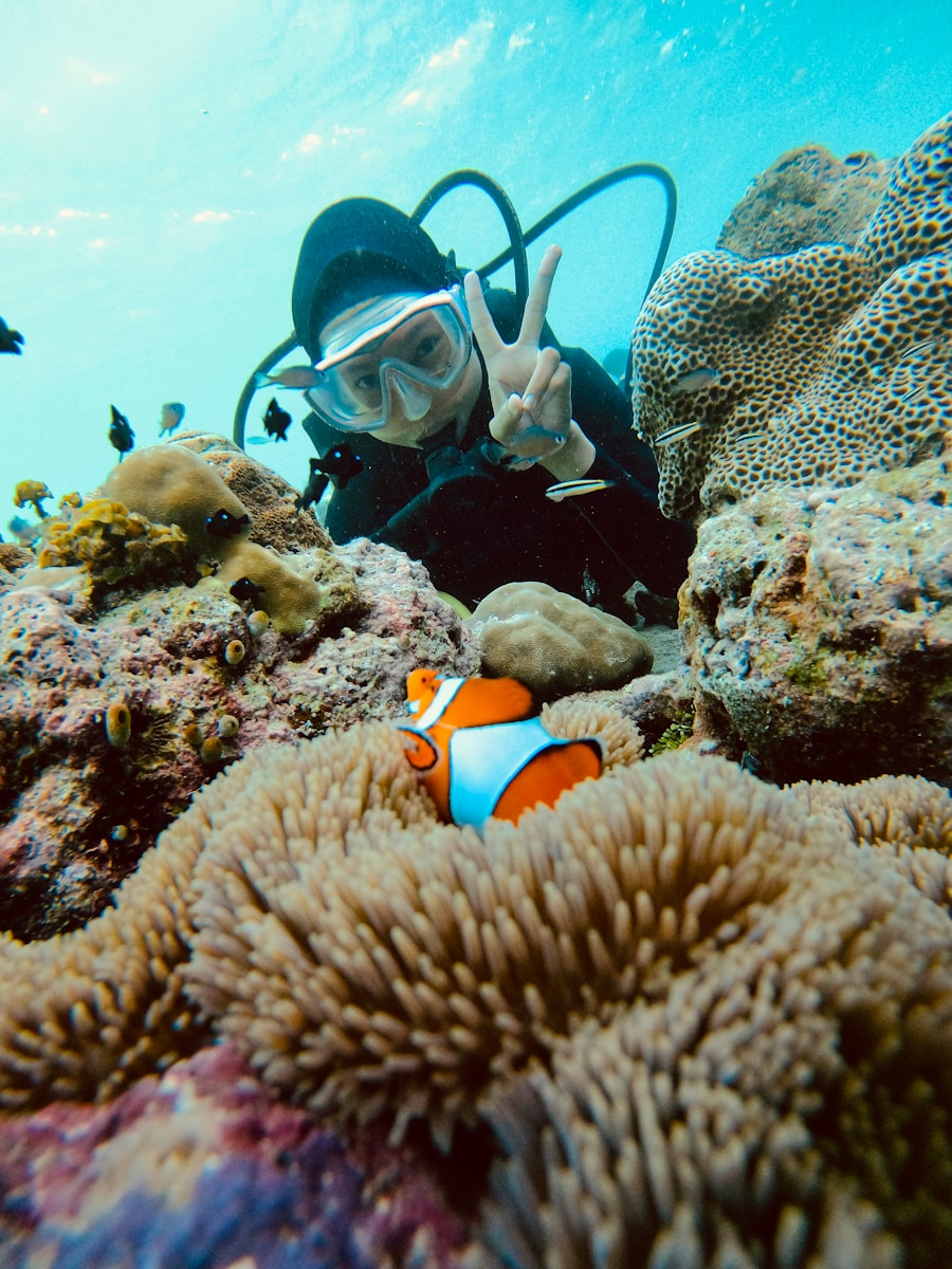 Scuba diver gives peace sign near clownfish and coral.
